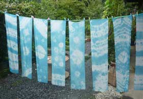 緑豊かな民家の庭先で開催された藍の生葉染め体験イベントにて　藍の生葉染めで空色に染まった絞りを施された絹の布が並んで干されているところ